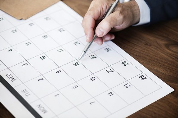 A hand holding a pen points to a date on the calendar chosen for office relocation